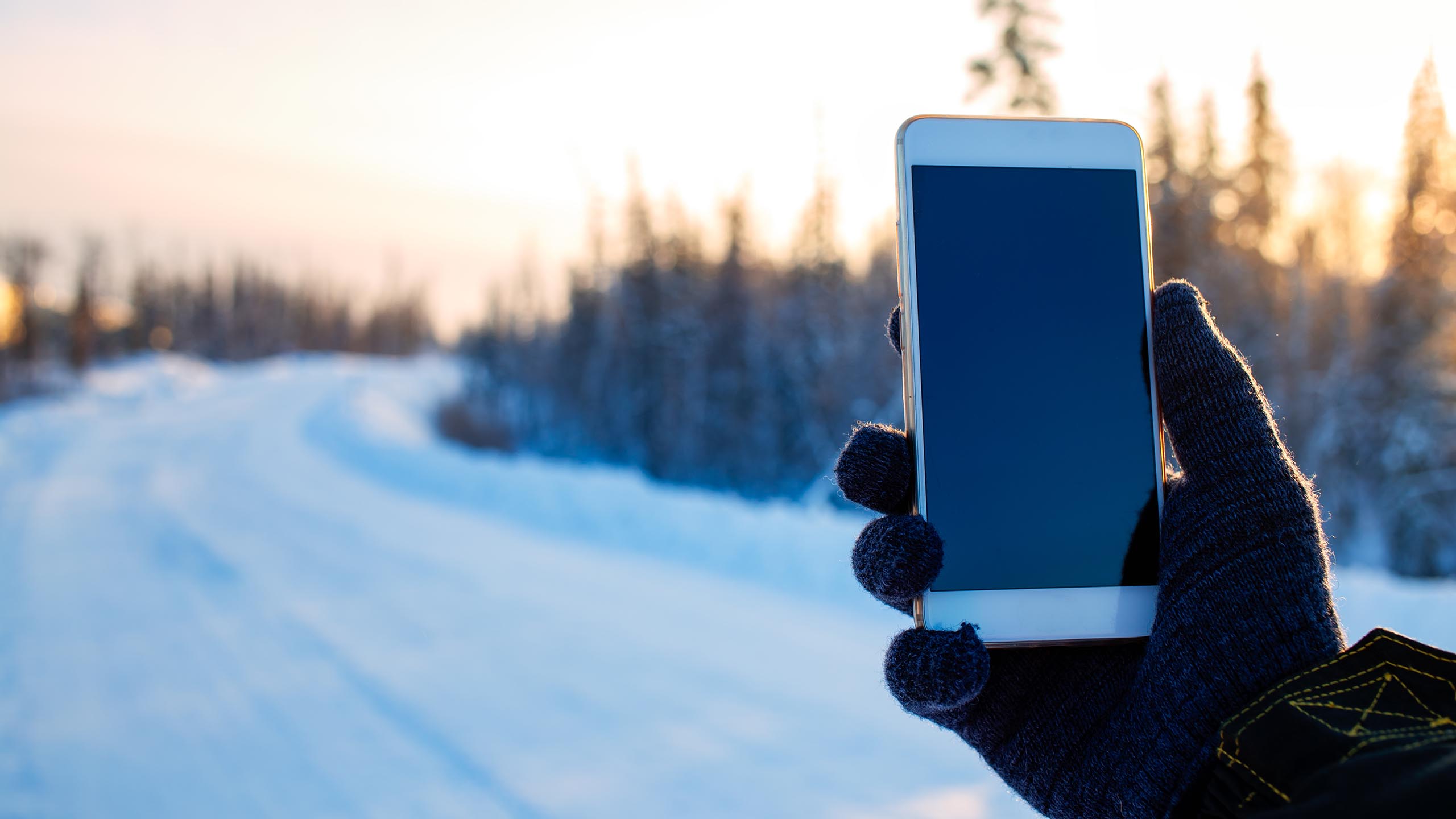 Närbild på en hand med en vante som håller i en mobiltelefon i ett vinterlandskap